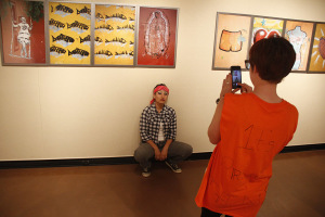 Cara Mack, math senior, takes a photo of Lucia Trejo, exercise physiology senior, in front of photgraphs taken by Gary Goldberg at the Faculty Art Exhibit on Oct. 31. Photo by Ethan Metcalf.