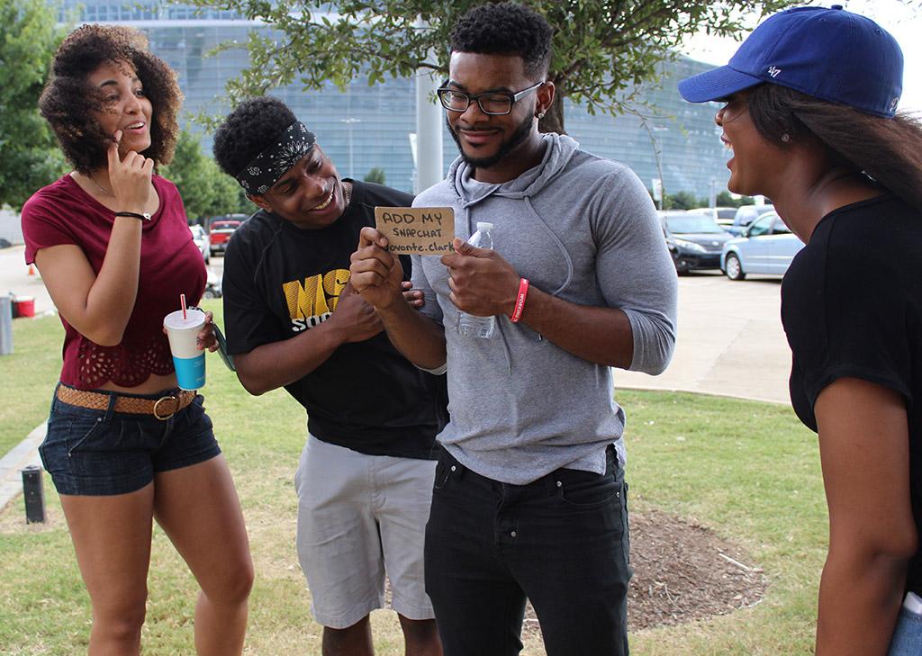 Jovonte Clark, alumni, holds a sign advertising his Snapchat account while tailgating outside the AT&T Stadium with Terrah Piggee, marketing senior, Simeon Nwegbo, alumni, and Michelle Blount, geology graduate student, Sept. 19. Photo by Rachel Johnson
