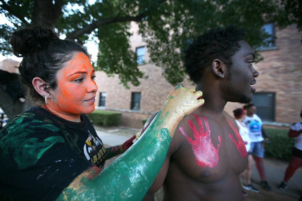 Aireanna Chavez, atheltic training freshman, paints the face of Austun Lambert, undecided freshman, in the Green Space where student painted each other  for the 2015 CaribFest Parade, Sept. 25. Photo by Bradley Wilson