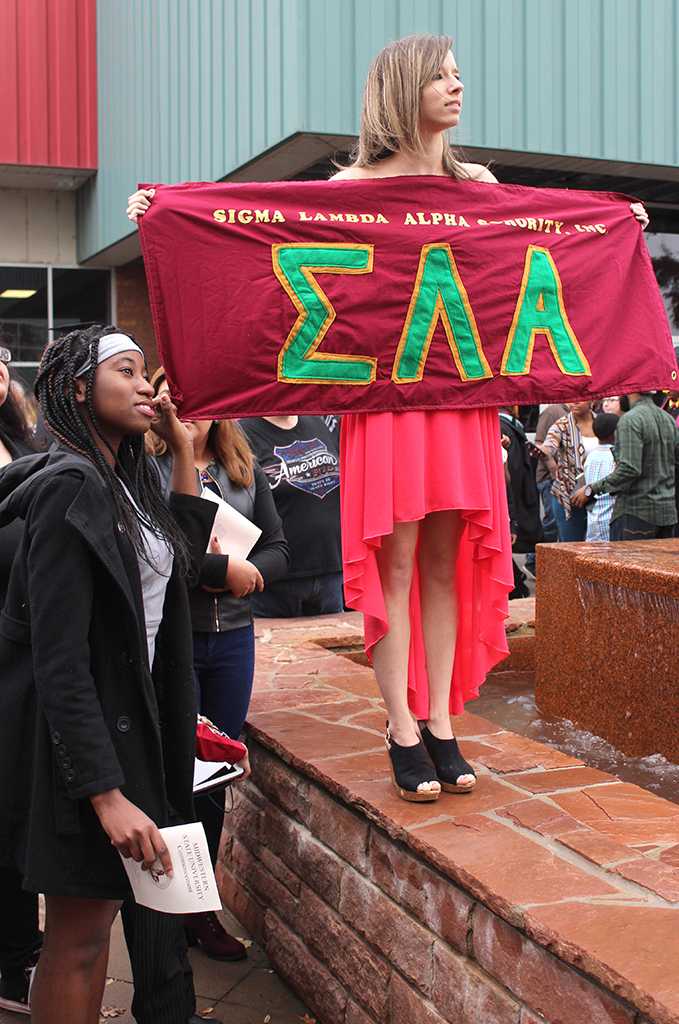Indira Placide, biology senior, and Krystal Basten, criminal justice junior, hold up a Sigma Lambda Alpha sign, so their two graduated sisters could find them after the ceremony, out side of the Kay Yeager Coliseum, Dec. 12. Photo by Rachel Johnson
