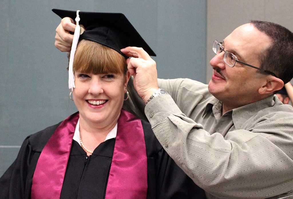 Sean Estrada helps his wife, Laura Estrada, English, put on her cap and fix her bangs while in the MPEC before Commencement Ceremony held in the Kay Yeager Coliseum, Dec. 12, where 440 crossed the stage. Photo by Rachel Johnson