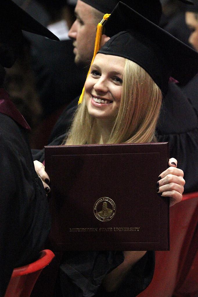 Emmi Wilson, criminal justice, holds up her diploma case so her mom in the audience could get a picture of her, in the Kay Yeager Coliseum, Dec. 12. Photo by Rachel Johnson