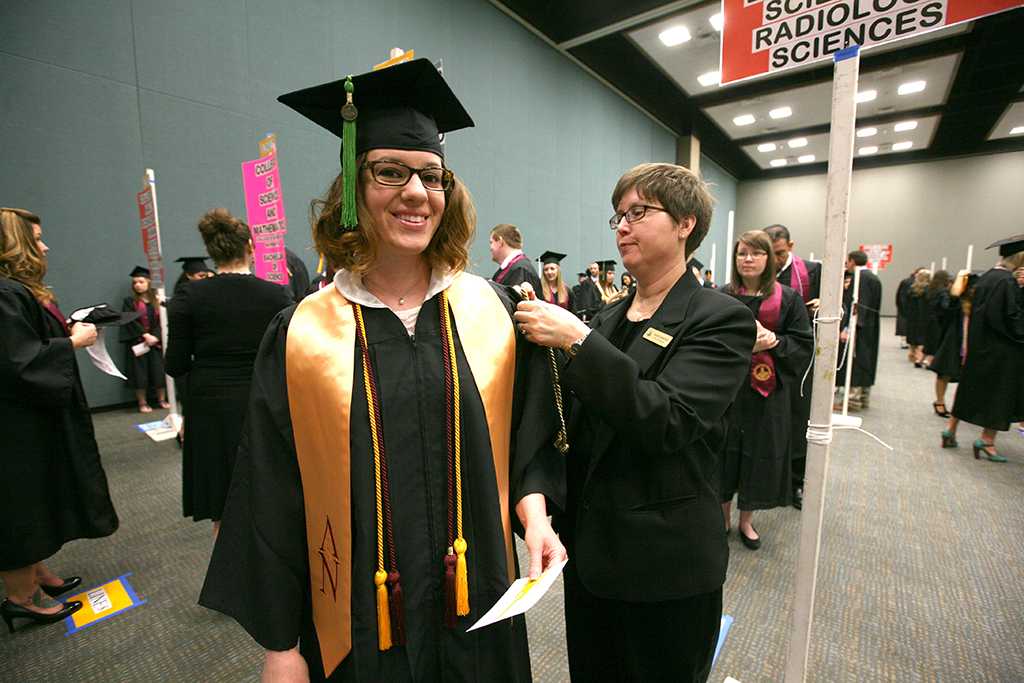 Bricelle Satterfield, office of registrar, helps Rachel Whatley, radiologic science, fix her gown at Midwestern State University graduation, May 16, 2015 at the Kay Yeager Coliseum. Photo by Rachel Johnson