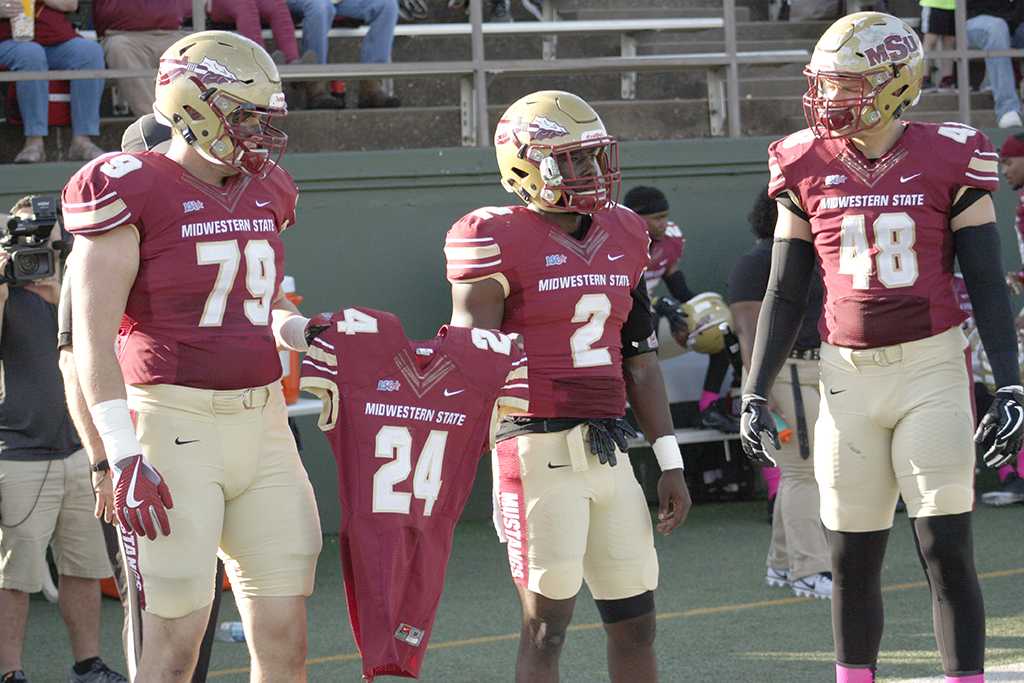 Kevin Fisher Jr., business managment junior, Sir'vell Ford, criminal justice junior, and Alec Divalerio, exercise physiology junior, carry the jersey of Robert Grays onto the field for the coin flip at the begining of the homecoming game where the Mustangs won 45-3 at Memorial stadium on Saturday, Oct. 21, 2017. Photo by Justin Marquart