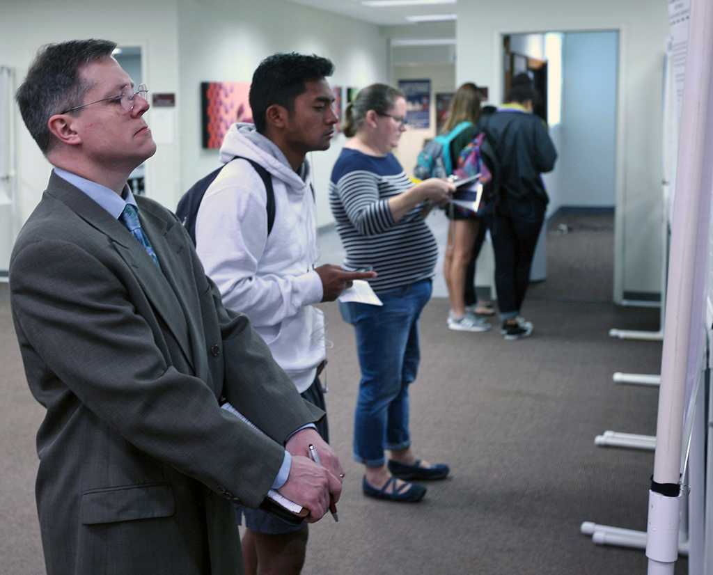 Dale Heidebrecht, Assistant Professor of Music and judge on Day2, examines and undergraduate student's poster.Celebration of Scholarship Faculty and Graduate Student Poster and Podium Presentations held at Atrium, Comanche Suites and Wichita Rooms, April 27.by Timothy Jones