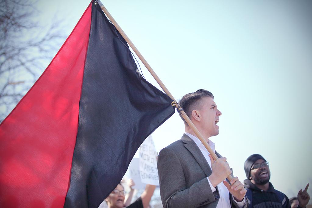 Nathan Jun, associate professor of philosphy, carries the flag of anarchism at the rally against the immigration executive order, on Feb. 1st. Photo by Bridget Reilly