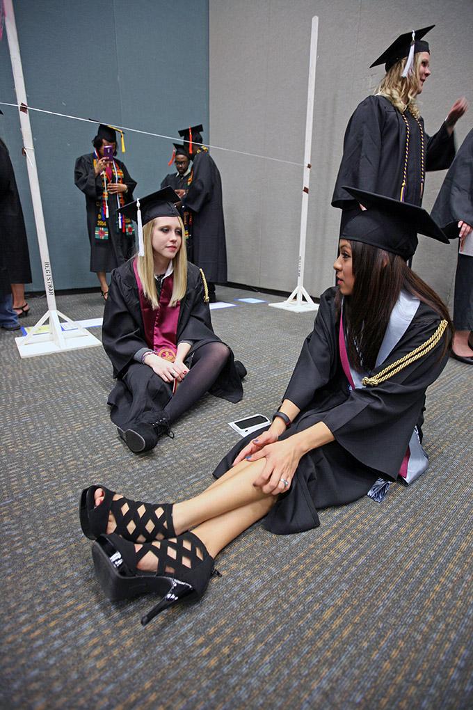 Bevin Pierce, psycology, and Sonia Perez, psycology, sit on the floor while they wait to be moved to the coliseum at Midwestern State University fall graduation, Dec. 13, 2014 in Wichita Falls, Texas. Photo by Rachel Johnson