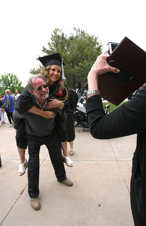 Chelsey Wall, special education, gets on her dad's back, Andrew Wall, for a piggy back picture after Commencement May 14, hed in the Kay Yeager Coliseum. Photo by Rachel Johnson