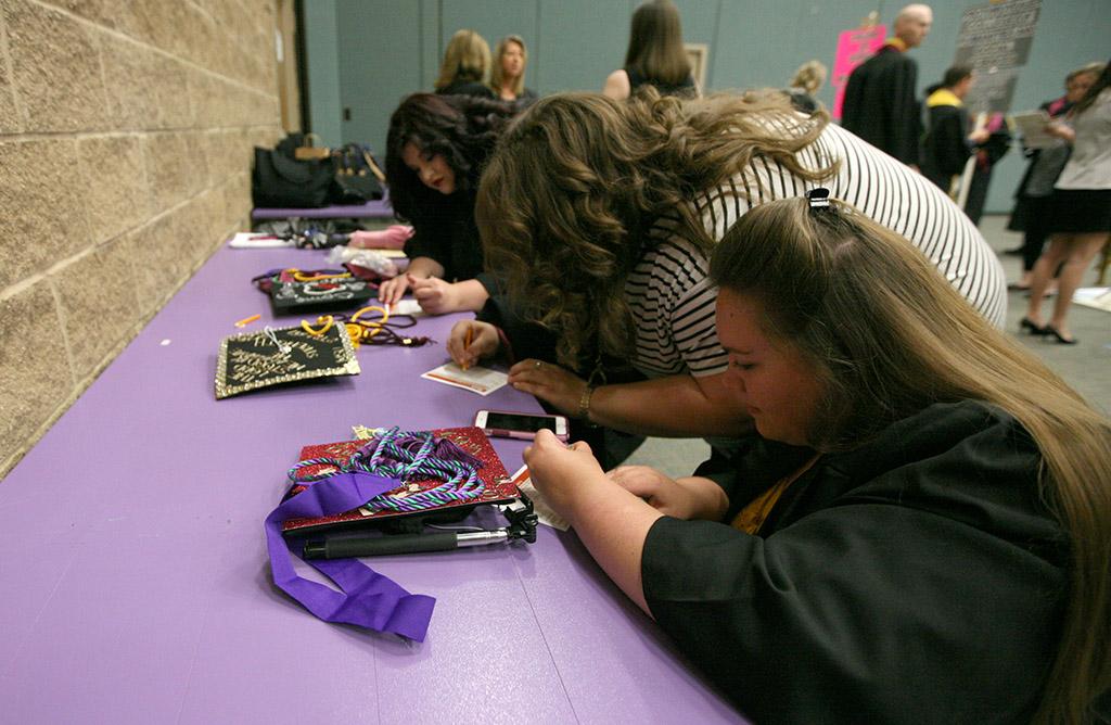 Holly Fachman, education, Shelby Ermis, education, and Bailee Fleming, music education, fil out their cards before getting in line with their departments before graduation, May 14. Each girl had a decorated hat for graduation, two of them went with disney for their inspiration, and the other went with her religion as the theme. Photo by Rachel Johnson