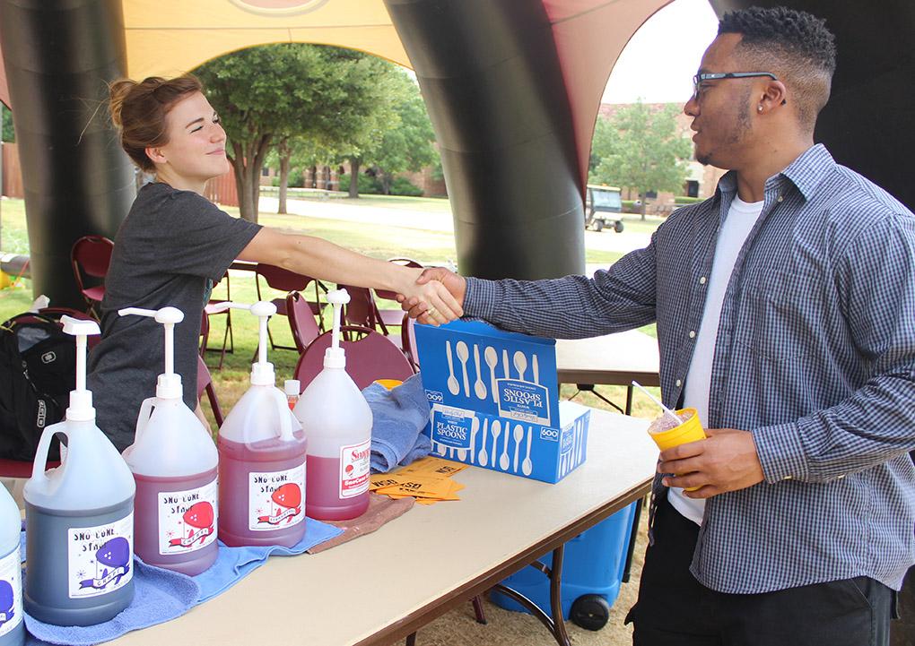 Ashley Burkhart, intern at the Baptist student Ministry, introduces herself to Tyre Browning, nursing freshman, at the free snowcone stand, provided by the BSM, under the big MSU tent on the greem space, during Move In Day Tuesday, August 18, 2015. Photo by Rachel Johnson