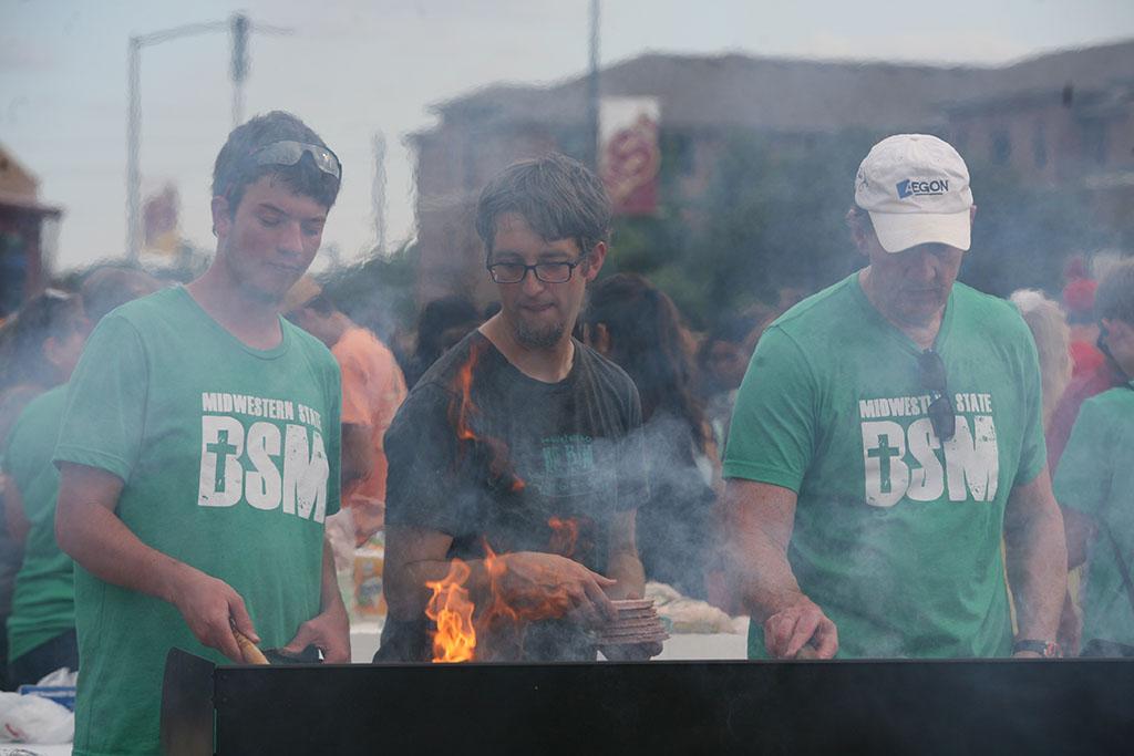 Jonathan Blassingame, radiology sophomore, Ben Edfeldt, director of the Baptist Student Ministry, and John Gill cook hamburgers. Photo by Bradley Wilson