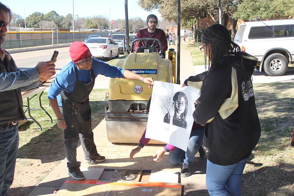 Lizca Bass, painting senior, hands Renee' Lonon, rider high school student, her print  at the Steamroller Print Event on Nocona Trial set up as a collaboration between MSU's Harvey School of Visual Arts and Wichita Falls Independent School District high schools, Feb 9, 2016. Photo by Francisco Martinez