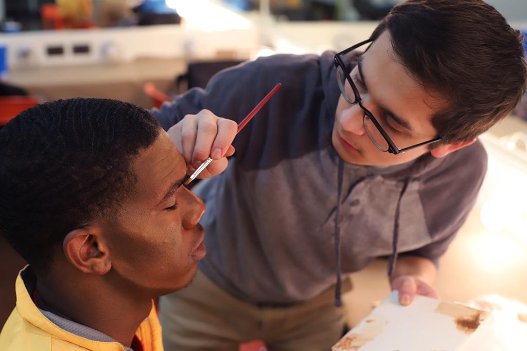 Kendall Jones learns how to apply his makeup for Urinetown from Christopher Cruz, head of makeup and Mr. McQueen, in the dressing room on Feb. 16, 2018. Photo by Sarah Graves