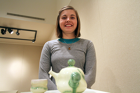 Chanda Droske, resident artist, stands behind a teapot and cup she made while setting up her exhibition in the Juanita Harvey Art Gallery. Droske's work will be displayed along with Mike Kern.  The opening will be this Friday at 6 P.M. Droske said," It's nice that people can use my work as well as admire it."