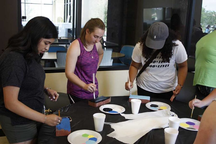 Joanne Ortega, mass communication sophomore, Miranda Schnitker, exercise physiology sophomore, and Melanie Garcia, exercise physiology sophomore, paint bricks at the brick painting event hosted by housing in Legacy hall on Aug. 22. Photo by Justin Marquart