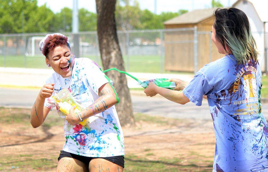 Amy Levy, biology sophomore, squirts her yellow team rival Zaquera Wallace, biology junior, with green paint during the Paint Fight held behind the Wellness Center, Friday April 6, 2018. Photo by Rachel Johnson