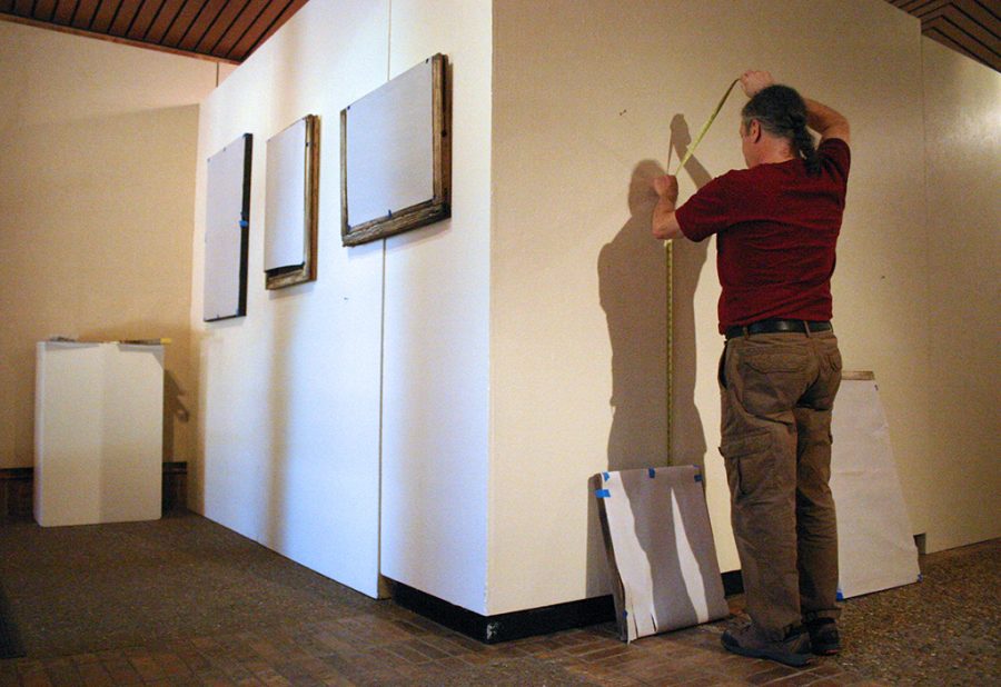 Gary Goldberg, art professor and gallery director, adjusts the placement of art pieces for the senior exhibition Thursday, May 2, 2018. Goldberg said that since there were so many graduating art students this semester, the artwork had to be displayed in the foyer, as well as the actual gallery. “We had to be more flexible this semester, but this space is mostly used as a path,” Goldberg said. “Our students often create pieces that challenge viewers emotionally and intellectually, so we have to create the galleries in a way that allows the viewer to make a choice if they want to engage in the art.” Photo by Brendan Wynne