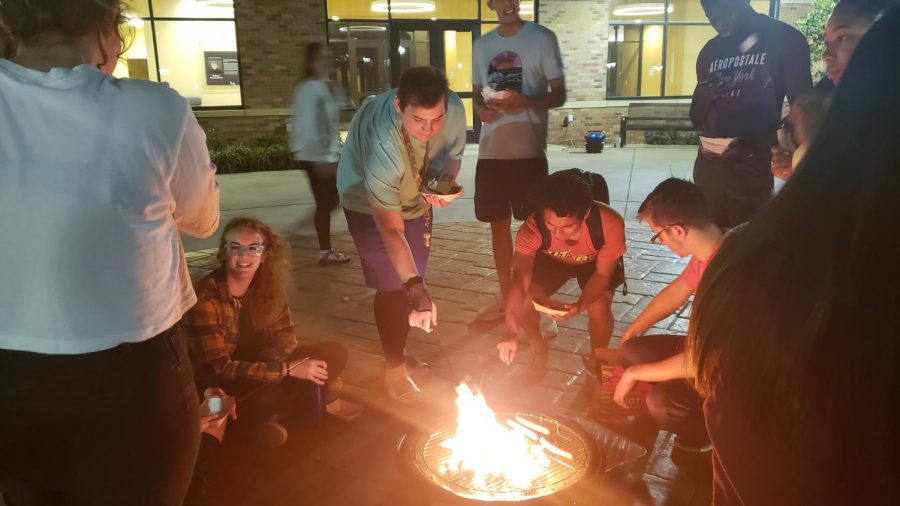 Students surround blazing firepit while roasting marshmellows.