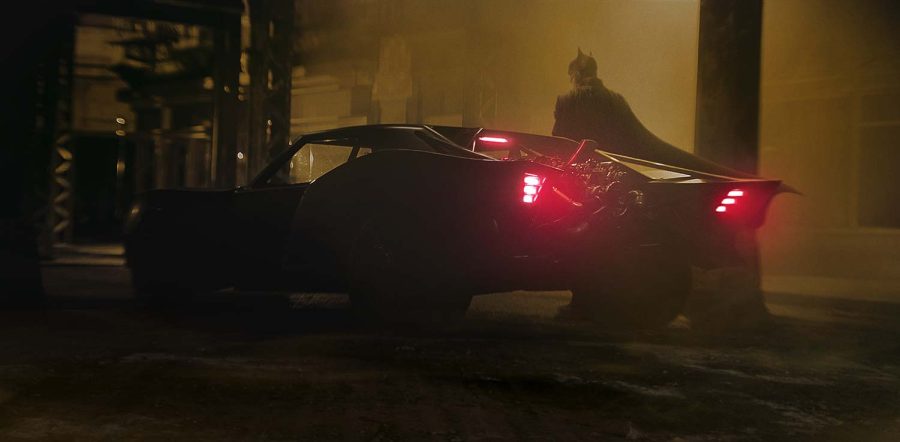 Batman stands belong his iconic car, showing its new design in The Batman, 2022.