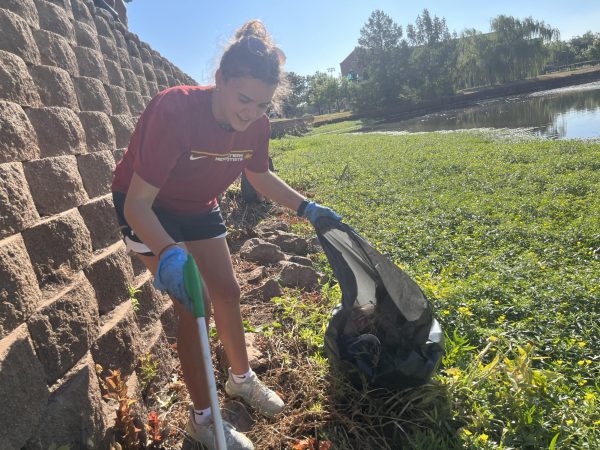 Macy Flowers, a physical education major, collects trash deep in the brush with her campus basketball team at MSUs Sikes Lake Cleanup initiative.